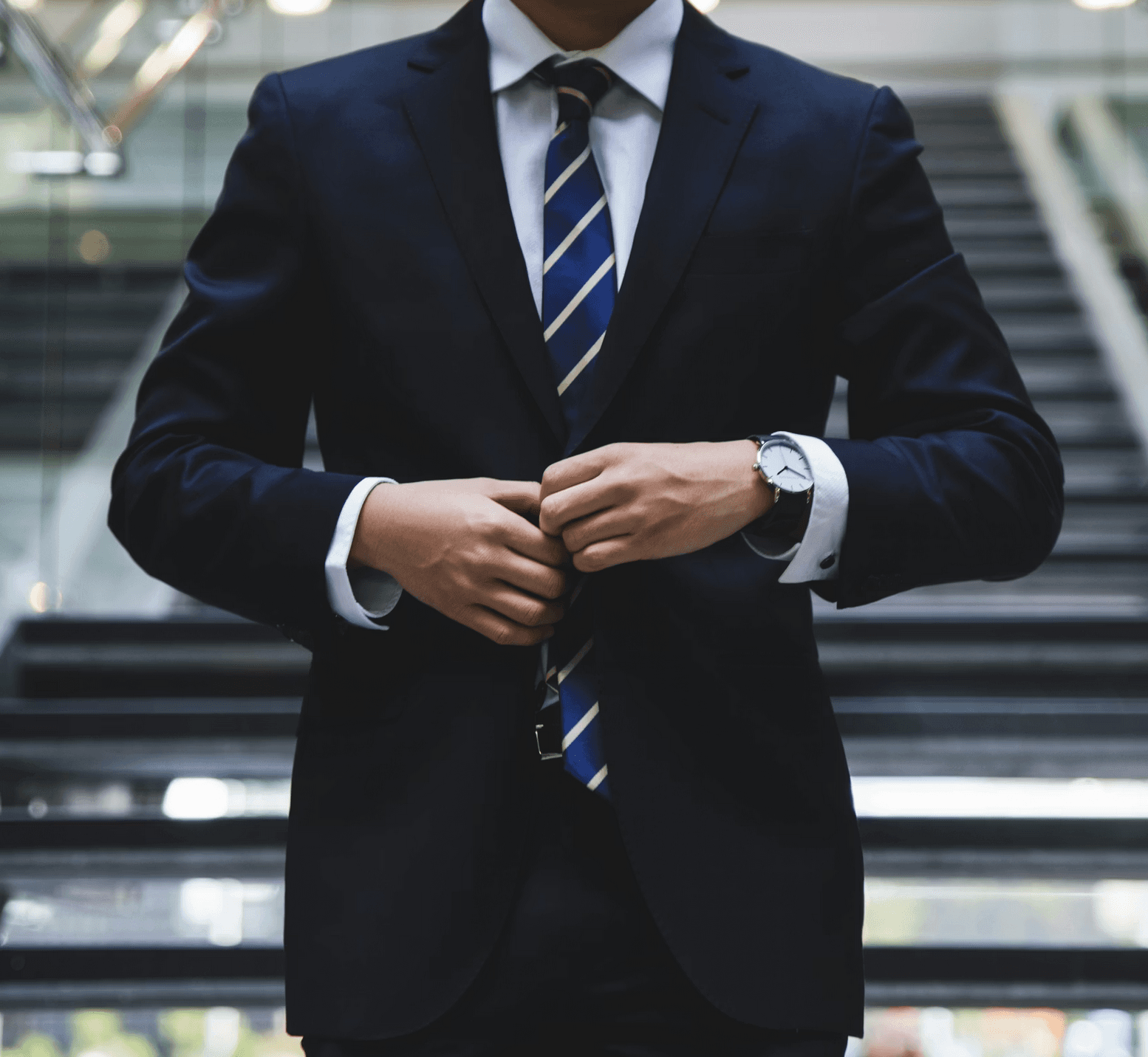 Businessman in a navy suit and striped tie buttoning his jacket in a modern office.