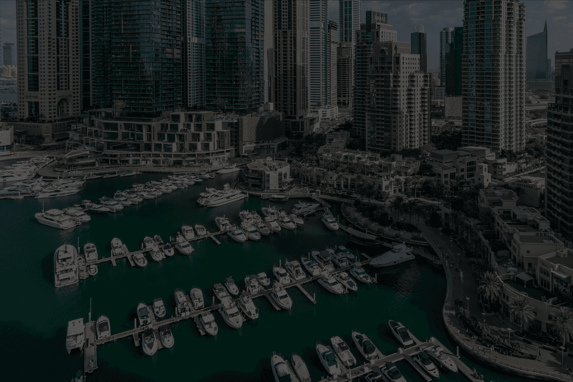 Aerial view of a marina with white yachts, surrounded by a dense skyline of skyscrapers.