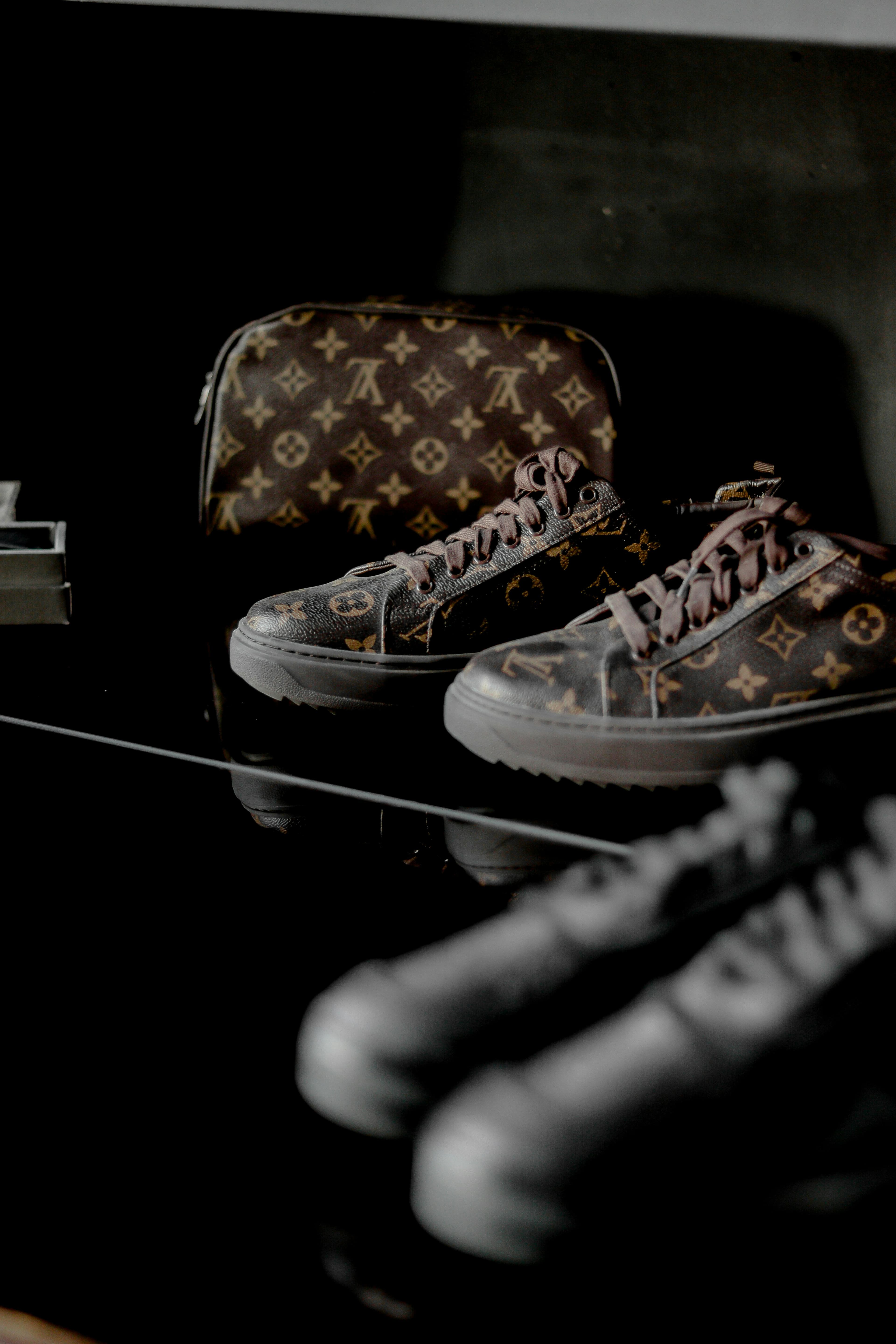 Louis Vuitton monogram sneakers and matching pouch on a dark, sleek reflective black surface.