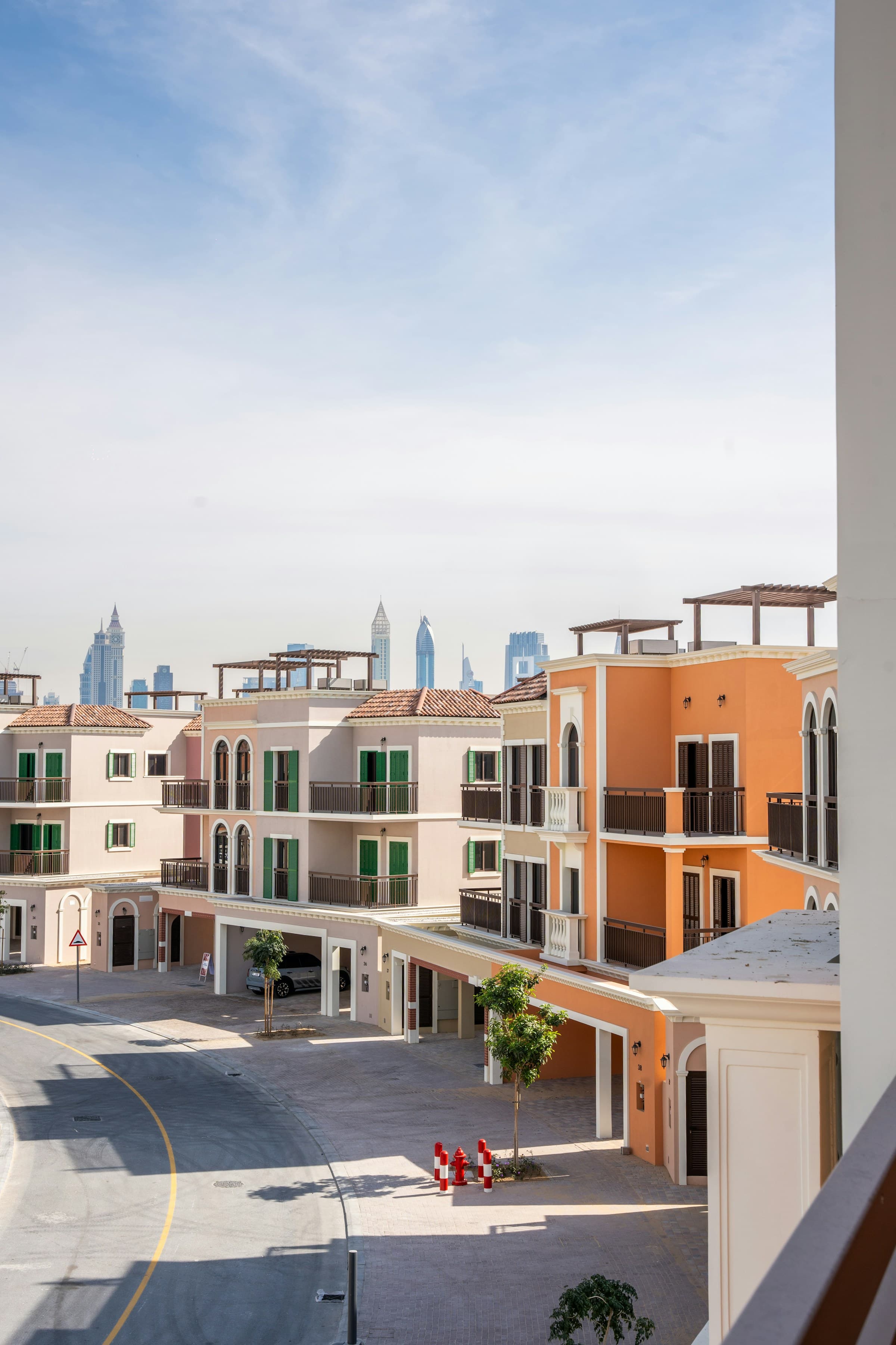 Mediterranean-style townhouses with peach facades and green shutters against a distant city skyline.