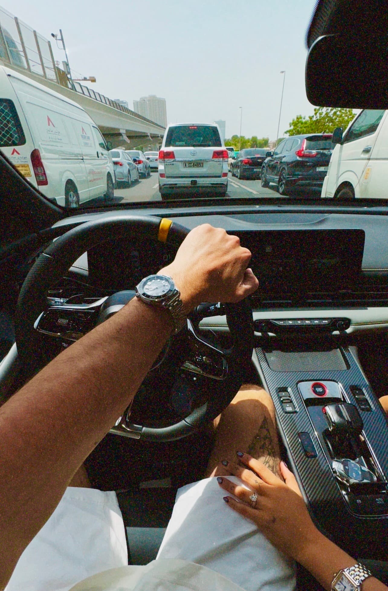 Driver's perspective of heavy traffic from a luxury car interior, featuring hands with luxury watches.