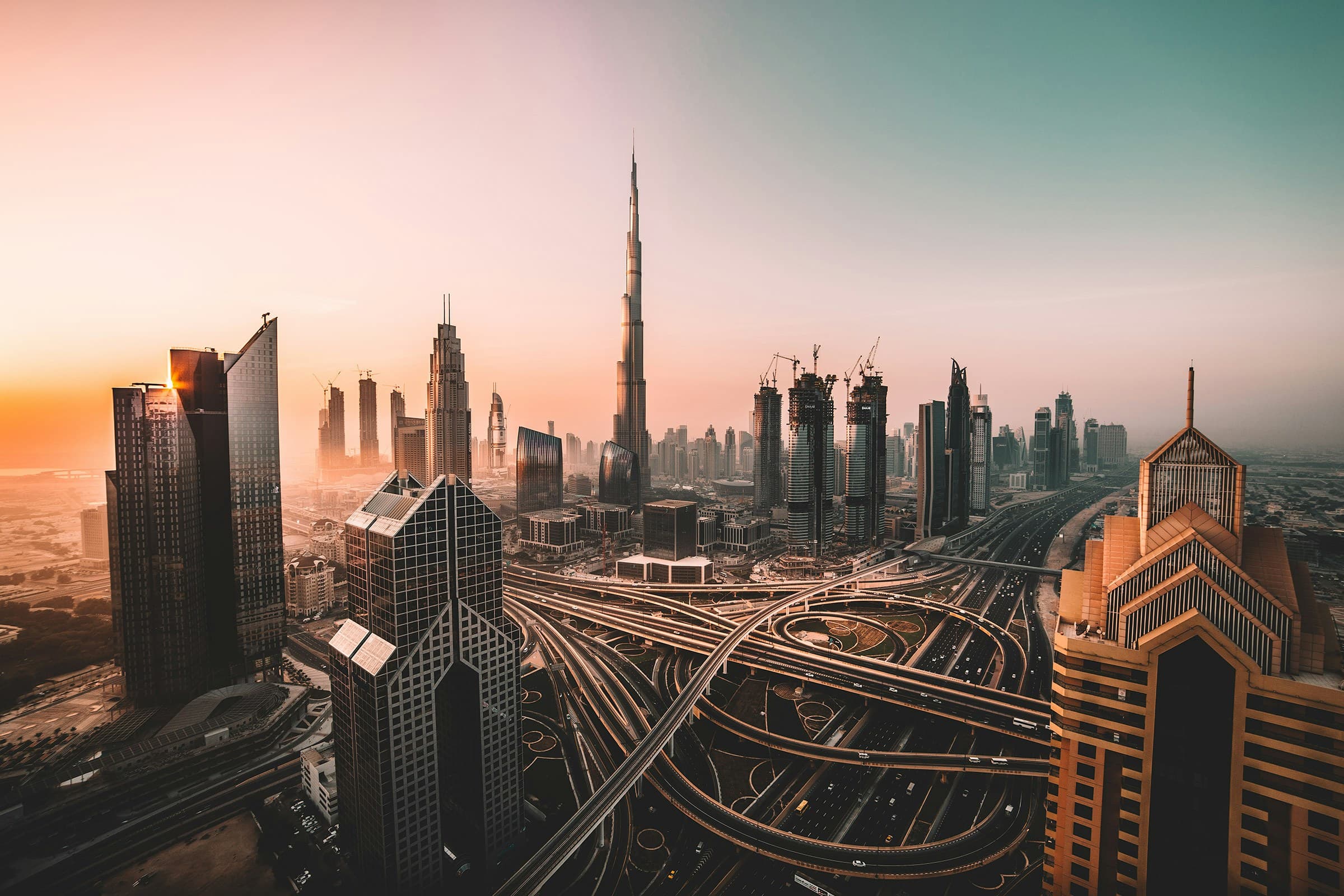 Sunset over Dubai's skyline featuring the Burj Khalifa and a complex network of highways.