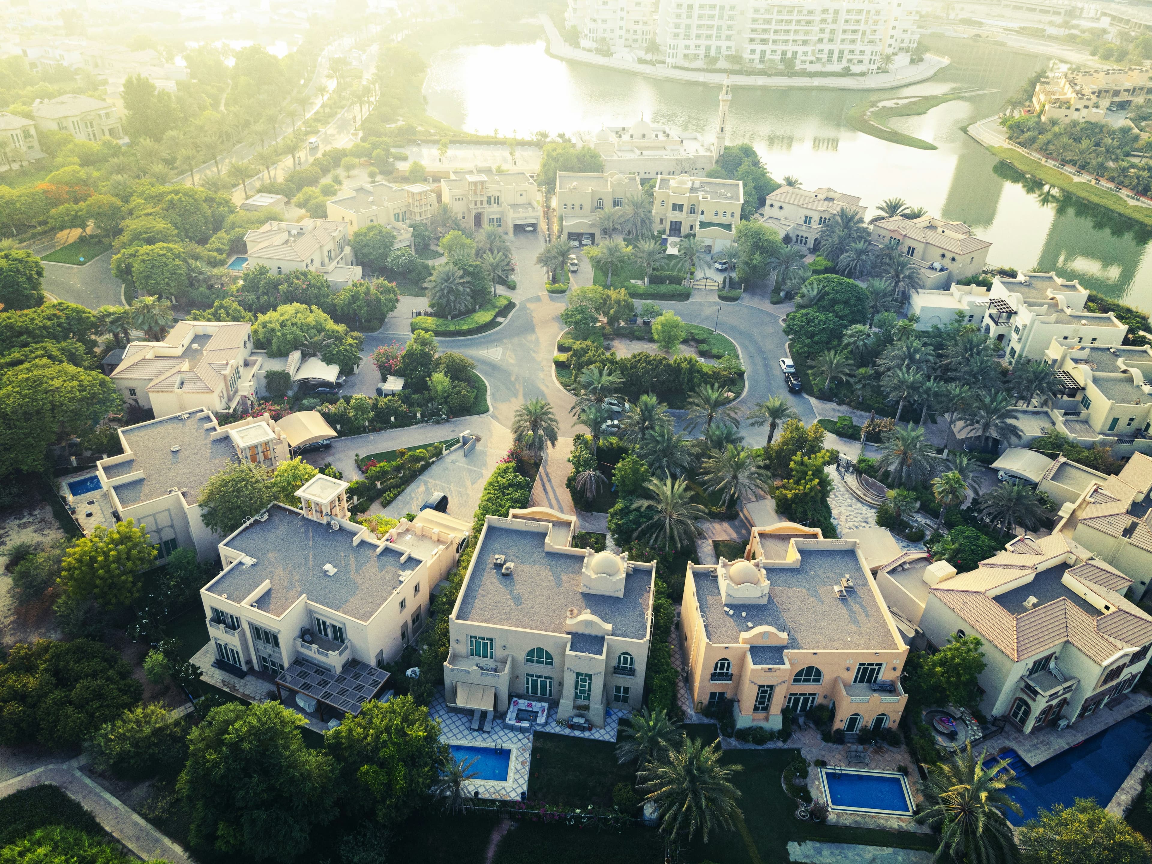 Sunlit aerial view of luxury villas and lush greenery in a waterfront residential neighborhood.
