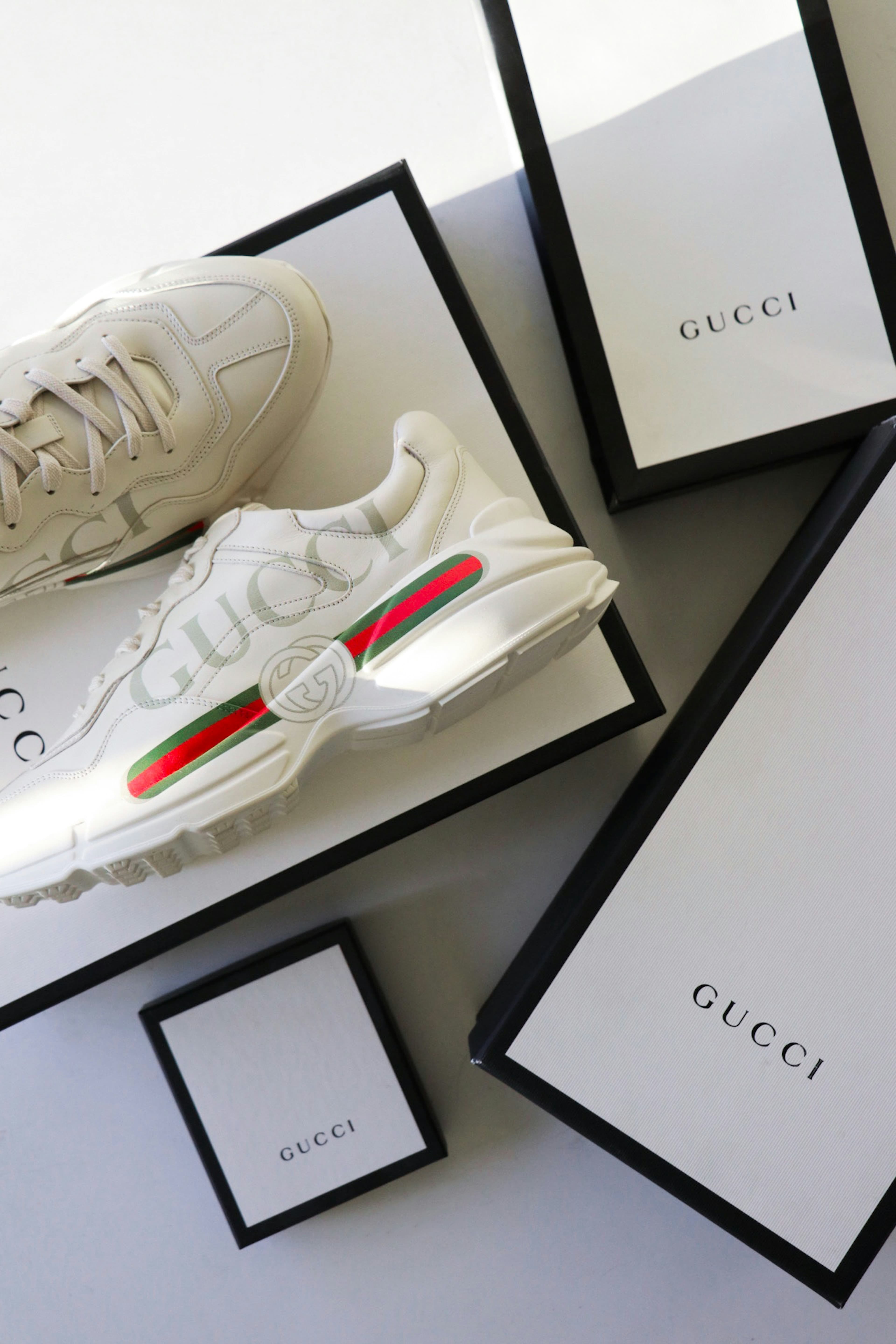 Chunky white Gucci sneakers with red and green stripes resting on branded luxury boxes.