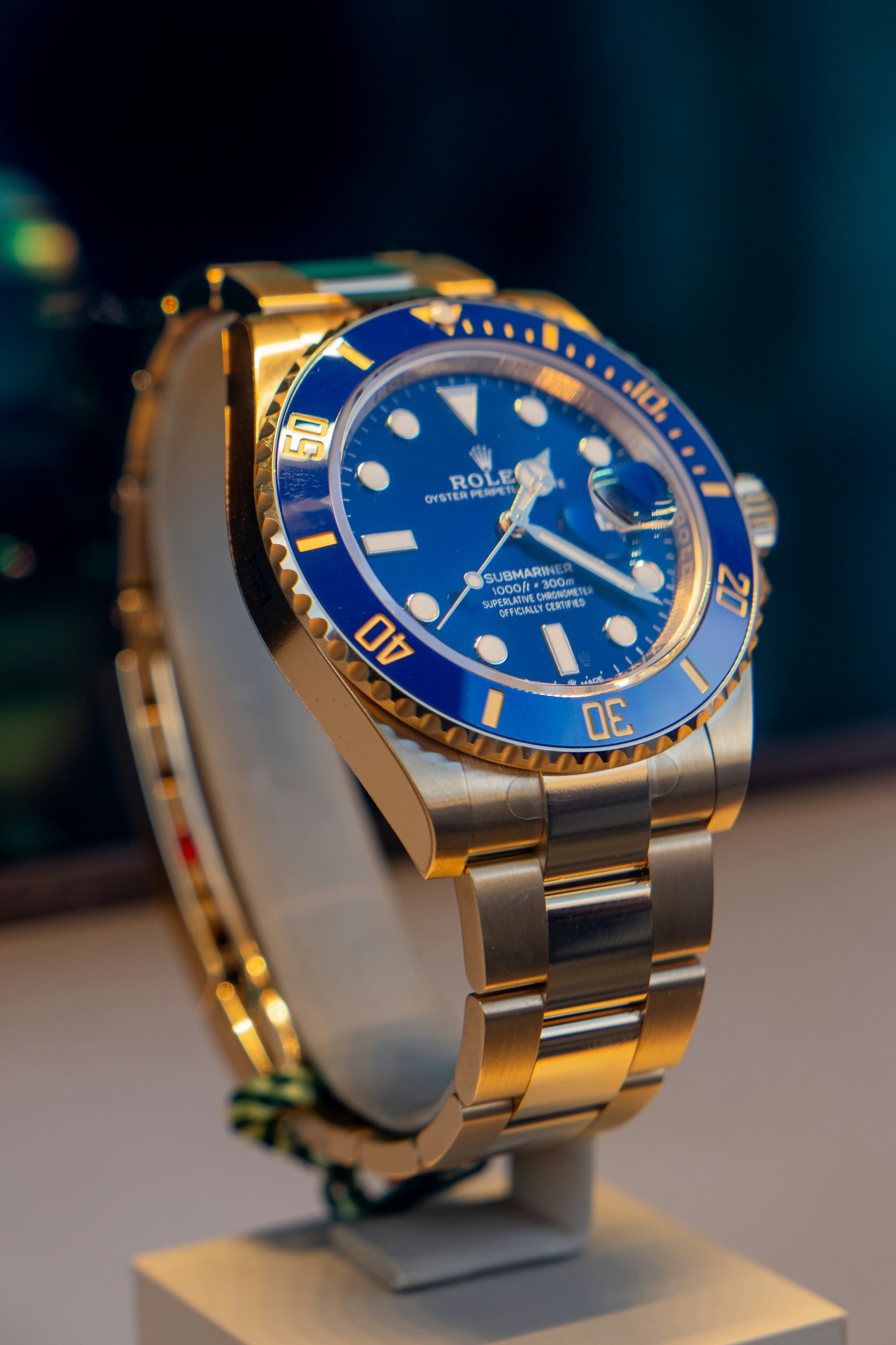 Gold Rolex Submariner watch with a blue dial and bezel on a display stand.